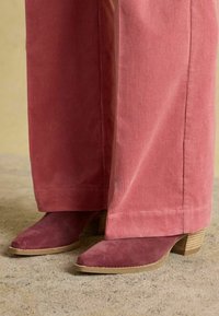 Rozā kordurojas plaša stila bikses ar teksturētu ribojumu, pasniegtas kopā ar bordo zamšādas potītes zābakiem ar smaili purngalu un sakrautu koka papēdi.