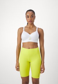 Witte sportbeha met verstelbare bandjes, voorzien van een mesh-paneel aan de voorkant. Felgele fietsbroek met zwarte accenten en een aansluitend ontwerp.