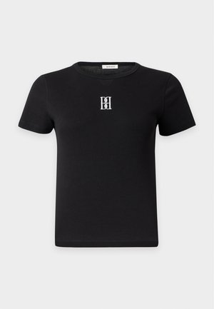 Donna in piedi di fronte che indossa una t-shirt nera aderente con un logo, una gonna midi beige con bottoni e scarpe basse bordeaux con lacci.