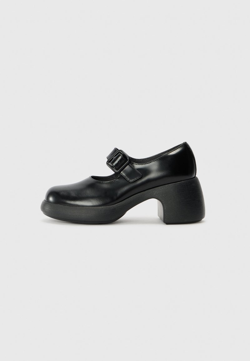 Black leather Mary Jane shoe with a round toe, adjustable buckle strap, and a thick, textured heel, featuring a smooth surface and minimal design.