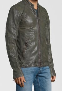 Kožená bunda v tmavě zelené barvě s přiléhavým střihem. Má přední zip, stojací límec a na boku zipovou kapsu.