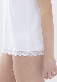 Haut en coton blanc avec un ourlet en dentelle festonnée. Le haut a des manches courtes et une coupe ample, mettant en valeur sa texture douce.
