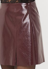 Burgundy faux leather minihame, jossa on kiiltävä pinta, sivu- Vetoketju ja hillitty halkio lisätietona. Sujuva tekstuuri kauttaaltaan.