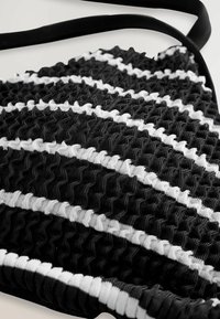 Borsa a tracolla a righe bianche e nere con design arricciato, dotata di una tracolla nera liscia. Il materiale sembra elastico e intrecciato.