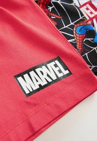 Roter Stoff mit einem schwarz-weißen Marvel-Logo-Patch neben einer Spider-Man-Grafik auf schwarzem Stoff mit weißem Netzmuster.