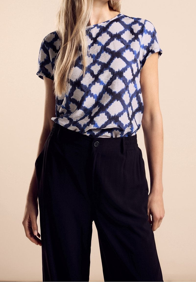 Blå och vit mönstrad kortärmad topp med en lös passform, tillsammans med svarta högmidjade byxor med en knapp och elastisk midja.