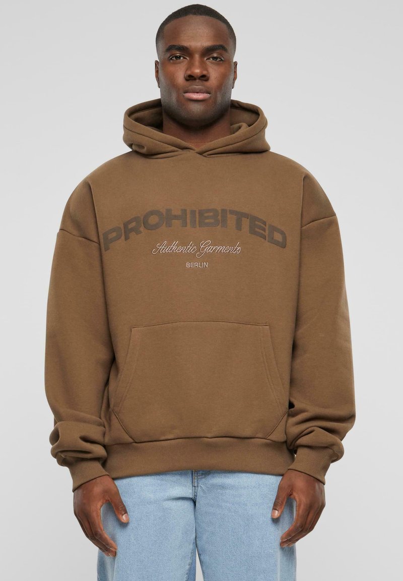 Brauner Kapuzenpullover mit dem Text "VERBOTEN", Kängurutasche, gerippten Bündchen und Saum, getragen über hellblauen Jeans.