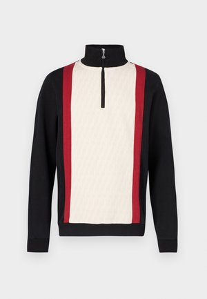 Pulôver com gola de meio fecho, com a parte da frente em creme com padrão, mangas pretas e riscas laterais vermelhas. Tecido texturado.