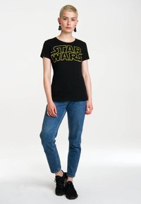 Black T-shirt featuring bold yellow "STAR WARS" text, paired with blue jeans and black sneakers. Simple design with a classic fit.