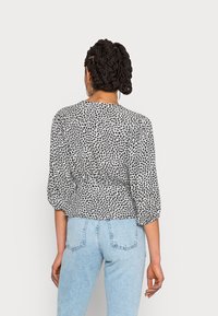 Svart- och vitmönstrad blus med trekvartsärmar, åtsittande midja och mjukt tyg, som kombineras med ljusblå jeans.