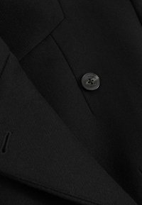 Blazer in lana nera con una texture liscia, rever affilati e un bottone nero lucido con design a quattro fori.