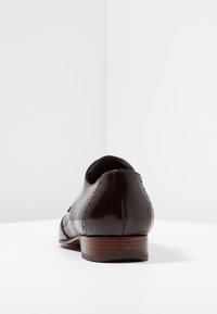 Chaussure en cuir verni noir avec un bout arrondi, des détails cousus et un talon en bois légèrement surélevé. Surface lisse avec une finition polie.