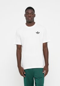 Hvid bomulds T-shirt med et lille sort Adidas-logo på venstre bryst. Korte ærmer og en rund halsudskæring med en klassisk pasform.
