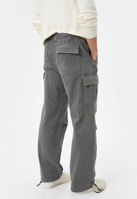 Pantalones cargo grises con cintura elástica, bolsillos laterales y parches traseros. El material es suave con un acabado mate; ajuste casual y holgado.