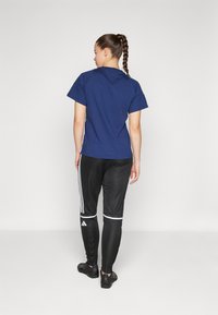 Marineblauwe katoenen T-shirt met korte mouwen, gecombineerd met zwarte sportbroek met witte strepen en logo, en zwarte schoenen.