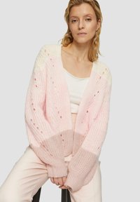 Gruba, dziergana cardigan w pastelowym różu i kremie, z detalami w otwartym splotzie i prążkowanymi mankietami. Luźny krój, lekka tekstura i oversize'owy design.