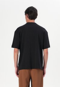 T-shirt noir à manches courtes en tissu doux, avec une coupe décontractée et un col rond. Design simple et minimaliste sans motifs.