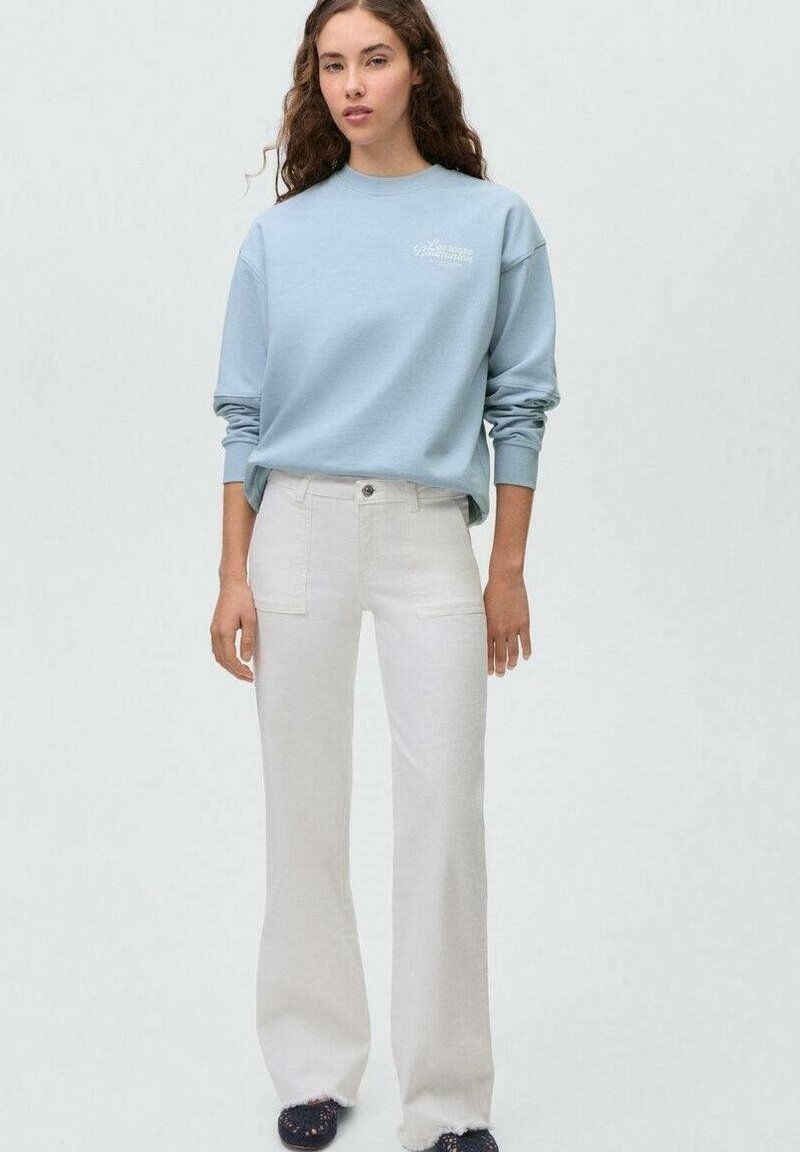 Felpa blu chiaro con scollatura rotonda e polsini a costine, abbinata a jeans a zampa off-white con tasche frontali e chiusura a bottone.