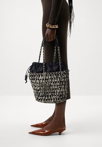 Woven black and white bucket bag with a drawstring closure, chain handles, and a soft black lining; structured shape and textured design.