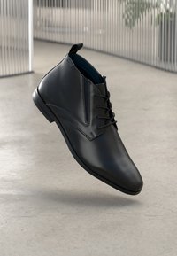 Schwarze Lederstiefeletten mit spitzem Schwanz, ausgestattet mit einer Schnürung auf der Vorderseite und subtilen Steppnähten, erhöhtem Absatz und glatter Textur.