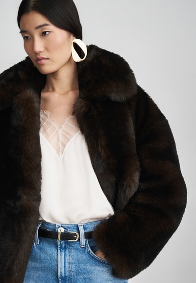 Palton din blană sintetică de culoare maro închis, cu o guler lat, purtat cu o bluză deschisă la culoare cu un model delicat stripe și blugi din denim albastri. Accent cu cataramă de curea aurie.