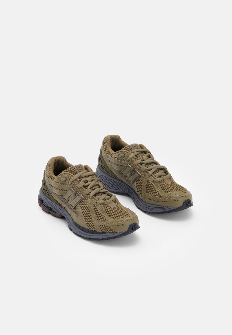 Paire de baskets de sport olive et grises avec tissu en maille et semelles épaisses et rembourrées sur fond blanc.