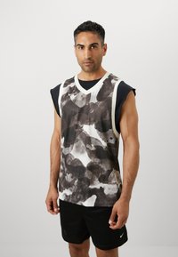 Jersey atlético sin mangas en blanco y negro, con patrones abstractos de manchas de tinta. Está hecho de una tela transpirable con un diseño de cuello en V.