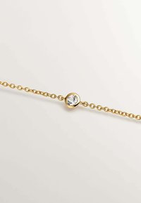 Pulsera de cadena de oro con una piedra redonda y clara engastada en un bisel liso. La cadena está compuesta por formas ovaladas unidas entre sí con un acabado pulido.