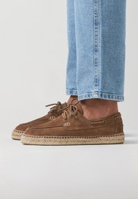 Bateaux en daim marron avec semelles en jute tressé, dotés de lacets ronds et d'œillets en argent. Assortis à un jean en denim bleu clair.