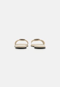 Beige sandals with a smooth, flat sole, thin straps, and a metallic buckle detail. The sole has a slight curve with a textured finish.