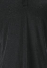 Svart polo skjorta i mjukt material med en strukturerad yta. Har en krage med dold knäppning och en liten logotyp på bröstet.