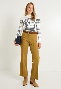 Haut à manches longues côtelé rayé blanc et marine, pantalon ample kaki, ceinture marron et bottines beiges, assortis à une pochette marine.