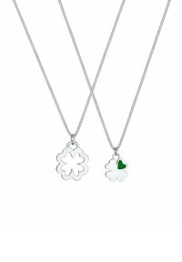 To sølv halskæder har en blomstret vedhæng, hvoraf den ene har et udskåret design, mens den anden har en lille grøn hjerteaccent.