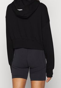 Svart, kort sweatshirt med huva, med en mjuk textur. Kombinerad med tajta svarta shorts som visar upp rena linjer och en minimalistisk design.