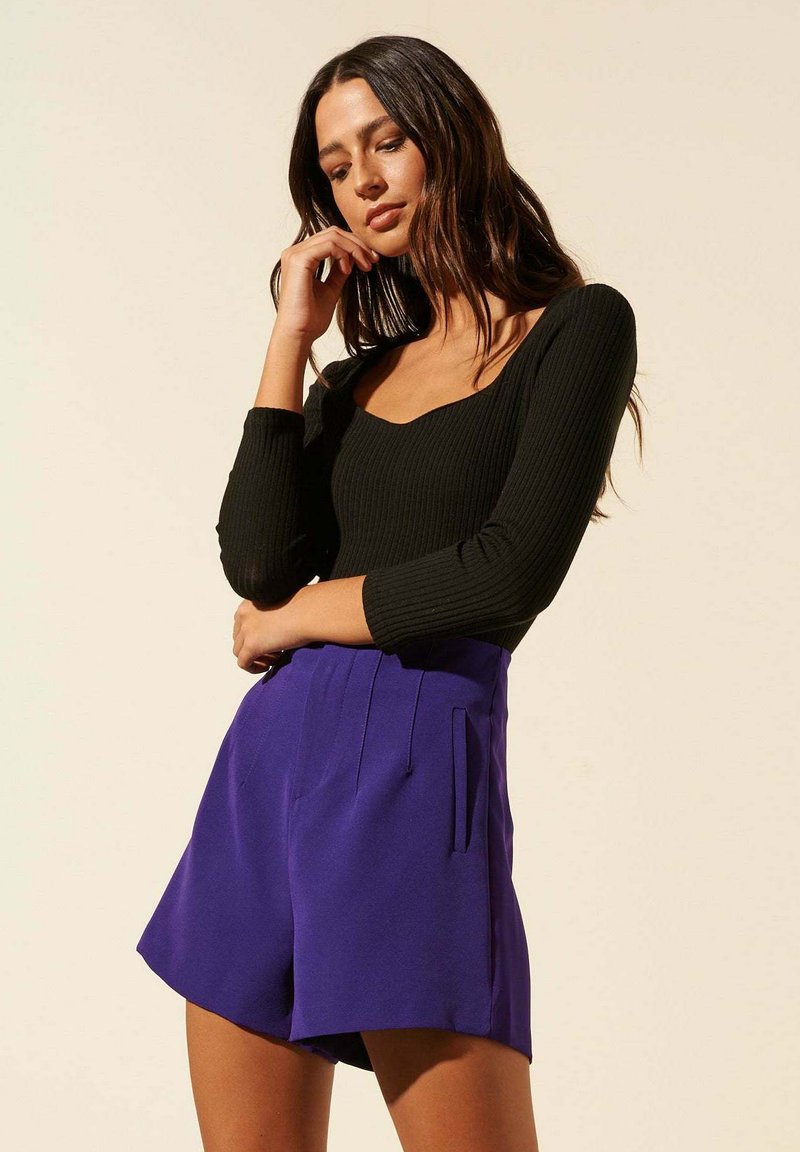 Bodysuit noir à côtes avec un décolleté rond associé à un short violet taille haute avec des plis et des poches latérales.