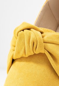 Primer plano de una tela amarilla suave que presenta un detalle de nudo texturizado en la parte superior de un zapato con forro interior beige.