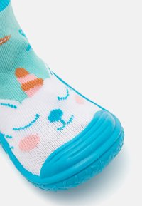 Bunte Kindersocke mit einem türkis-weißen Design, das ein lächelndes Tiergesicht zeigt, aus strukturiertem Stoff gefertigt und mit einer gummierten Sohle.