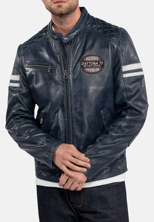 Mørkeblå læderjakke med lynlås, quiltede skulderdetaljer, broderet logo og stribede detaljer på ærmerne.