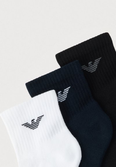 Trzy pary prążkowanych skarpet w kolorach czarnym, granatowym i białym, z logo w postaci poziomych pasków na każdym ściągaczu.