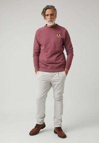 Sudadera marrón con cuello redondo y logo gráfico, combinada con pantalones gris claro y botas de cordones marrones. Tejido suave y corte relajado.