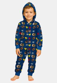 Bambino in piedi a piedi nudi che indossa una tuta con cappuccio blu con un motivo di facce di cani cartoni animati colorati, stelle, fiamme e chiavi inglesi.