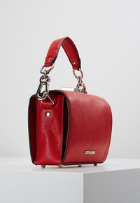 Sac à main en cuir rouge avec une finition texturée, des ferrures en argent, une bandoulière amovible et une forme rectangulaire, agrémenté d'un détail métallique de marque.