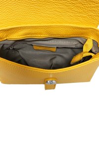 Interno di una borsa a tracolla in pelle gialla con una tasca con zip e un piccolo scomparto in tessuto beige. Superficie testurizzata con chiusura a scatto in metallo.