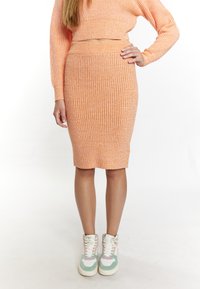 Orangenes geripptes Strick-Zweiteiler-Outfit, bestehend aus einem cropped Pullover und einem Bleistiftrock, kombiniert mit weißen und mintgrünen High-Top-Sneakern.