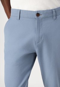 Pantaloni de culoare albastru deschis, realizați dintr-un material texturat, având închidere cu nasture, buzunare laterale și un design drept.