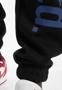Black sweatpants with elastic cuffs featuring a blue logo. Paired with red and white sneakers featuring a distinctive design.