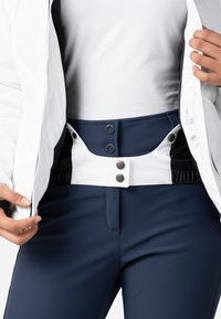 Námořnické lyžařské kalhoty s bílým pasem se dvěma černými patentkami. Tkanina je hladká, elastická a navržená pro aktivní nošení.