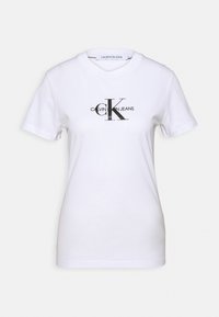 Krátký rukáv, bílý bavlněný tričko s kulatým výstřihem. Obsahuje černě tištěné logo "CALVIN KLEIN JEANS" a velké "CK" ve středu.