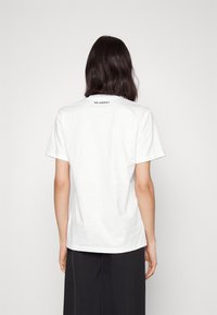 Bílá krátká sloupcová tričko, bavlněný materiál, s kulatým výstřihem. Na zadní straně je vytištěno "KARL LAGERFELD" černou barvou. Jednoduchý, volný střih.