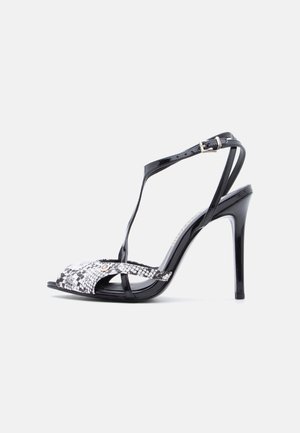 Sandale noire à talon haut avec bride autour de la cheville et boucle argentée, présentant un motif texturé peau de serpent sur les orteils.
